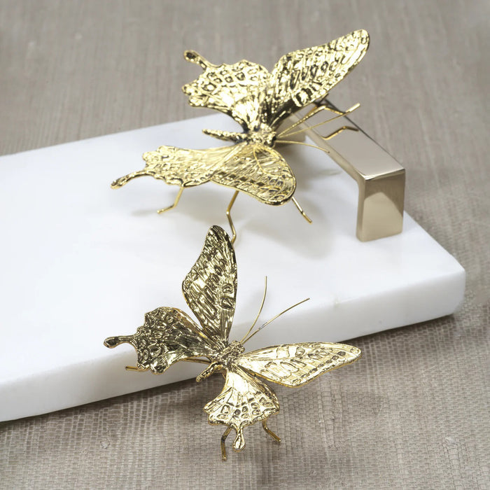 The ZODAX DECORATIVE ANTIQUE GOLD BUTTERFLY - SMALL is a gold-colored zinc alloy sculpture with textured wings and six thin legs. Displayed on white, it measures 3.25" x 2.5" x 1.5".