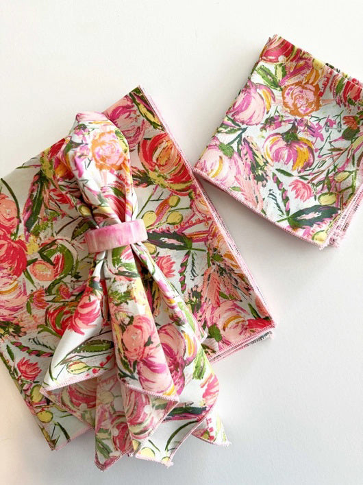 Three DOT AND ARMY FLORAL FROLIC DINNER NAPKINS in pastel pink, green, and yellow floral patterns are shown on a white surface—super soft, one is folded with a fabric napkin ring while two are stacked.