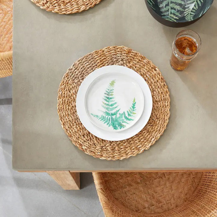 The NAPA HOME AND GARDEN - SEAGRASS ROUND PLACEMAT, featuring a textured, natural brown color, beautifully complements the elegance of Italian ceramics on a white background.