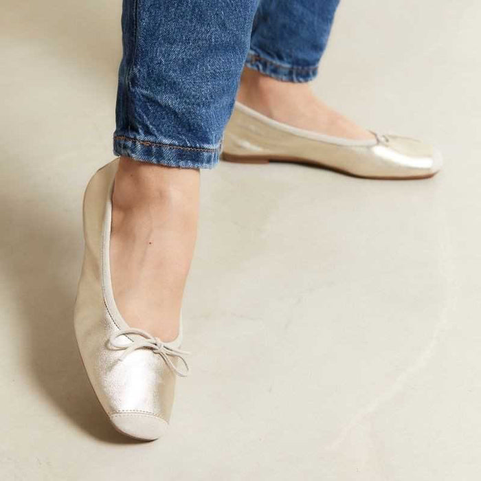 A top view of the REQINS Harmony Bellerina Flat in metallic platinum, featuring a small toe bow and crafted from metallic leather, displayed on a plain light background.