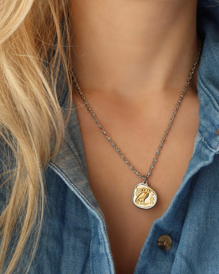 Woman wearing a silver coin pendant necklace with Athena's Owl of Wisdom, a replica of an ancient Greek Athenian tetradrachm coin that is silver with a gold owl, two-tone mixed metal necklace made in Greece on an infinity s-link chain