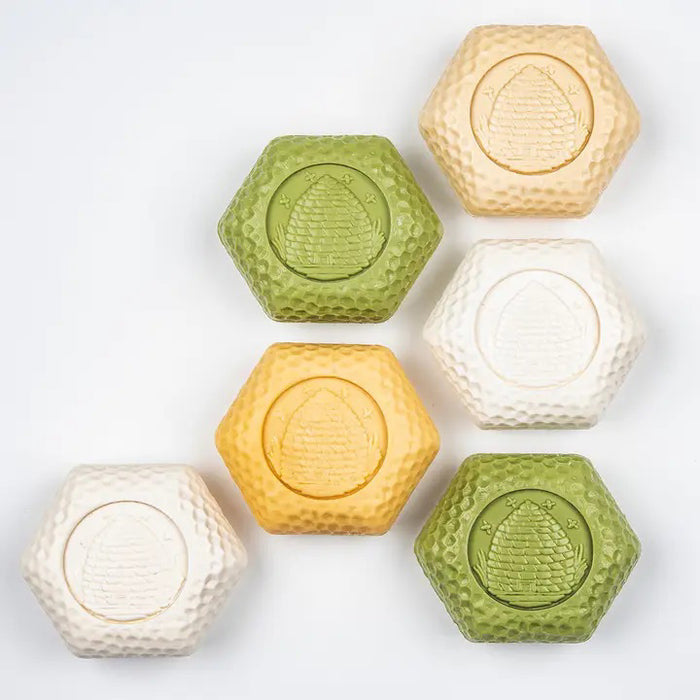 A beautifully designed BAUDELAIRE - GOATS MILK HONEY SOAP 1.4oz Gift Box features eight hexagonal white soaps arranged in an open grid, topped with a floral-patterned lid. These moisturizing BAUDELAIRE soaps are ideal for sensitive skin, providing gentle care with every use.