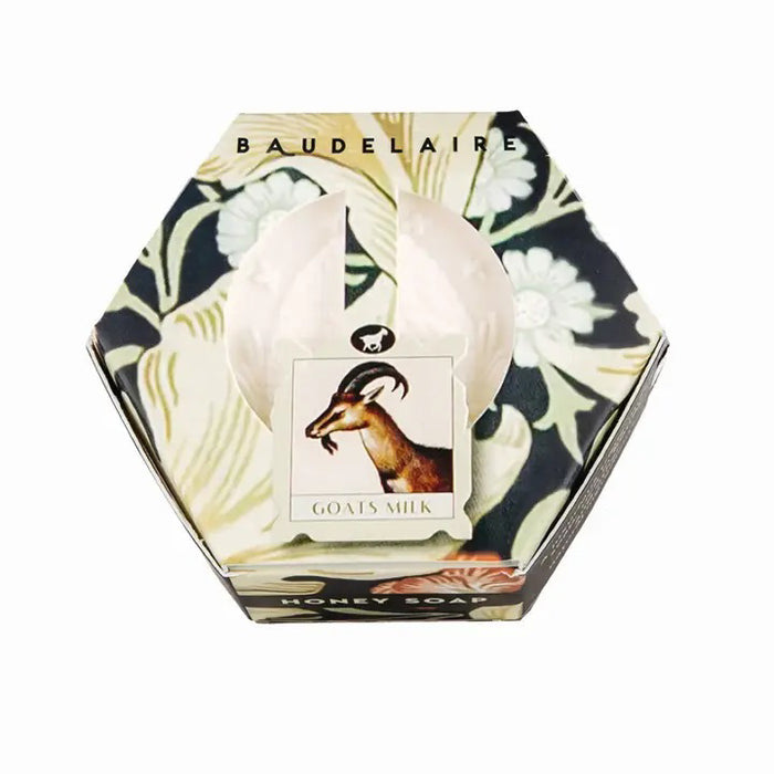 The BAUDELAIRE - GOATS MILK HONEY SOAP HEX BOX 3.5OZ comes in a hexagonal box adorned with a delicate floral motif and features a central label illustrated with a goat. Gentle enough for sensitive skin, this moisturizing soap is visible through an opening in the packaging.