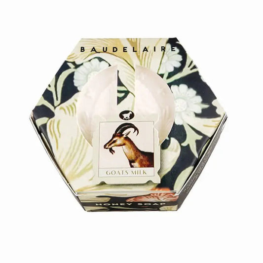 The BAUDELAIRE - GOATS MILK HONEY SOAP HEX BOX 3.5OZ comes in a hexagonal box adorned with a delicate floral motif and features a central label illustrated with a goat. Gentle enough for sensitive skin, this moisturizing soap is visible through an opening in the packaging.