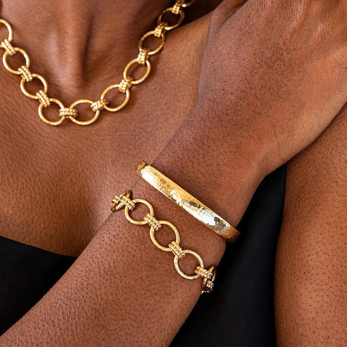 The CAPUCINE DE WULF - CLEOPATRA OVAL HINGED BANGLE SMALL/MEDIUM is a polished, hammered gold bracelet, expertly handcrafted by CAPUCINE DE WULF and displayed against a plain white background.