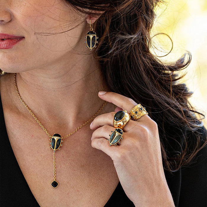 The CAPUCINE DE WULF Scarab Petite Drop Blue Labradorite/Black Agate Earrings feature beetle-inspired designs with black and blue stones and six blue gems—unique statement jewelry for a striking look.
