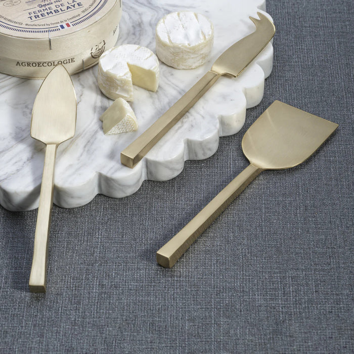 The ZODAX CHEESE SLICER AND SERVER SET includes three gold-toned cheese knives—flat spatula, chisel, and fork-tipped—each with rectangular handles, displayed side by side on a white background.