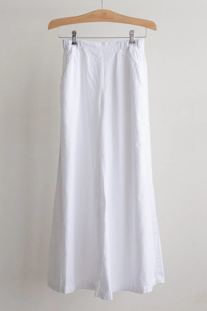 The CP SHADES - WENDY PALAZZO PANT is a pair of loose-fitting, high-rise blue cotton wide-leg pants with an elastic waistband, displayed on a wooden hanger against a plain white background.
