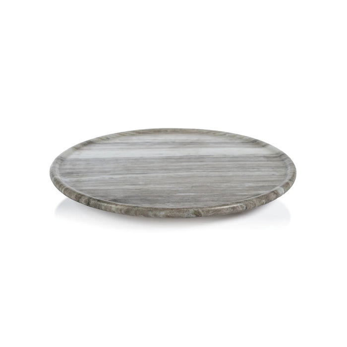 The ZODAX CREMA MARFIL MARBLE LAZY SUSAN, a round 16-inch grey and white serving platter, sits on a textured grey surface with a gold-colored metal spatula resting at its edge.