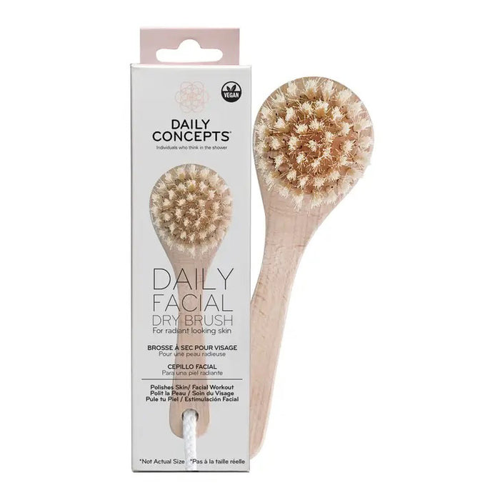 A DAILY CONCEPTS FACIAL DRY BRUSH with a wooden handle and natural bristles is displayed in front of its packaging, labeled for gentle exfoliation and radiant skin. The package shows product details and icons.