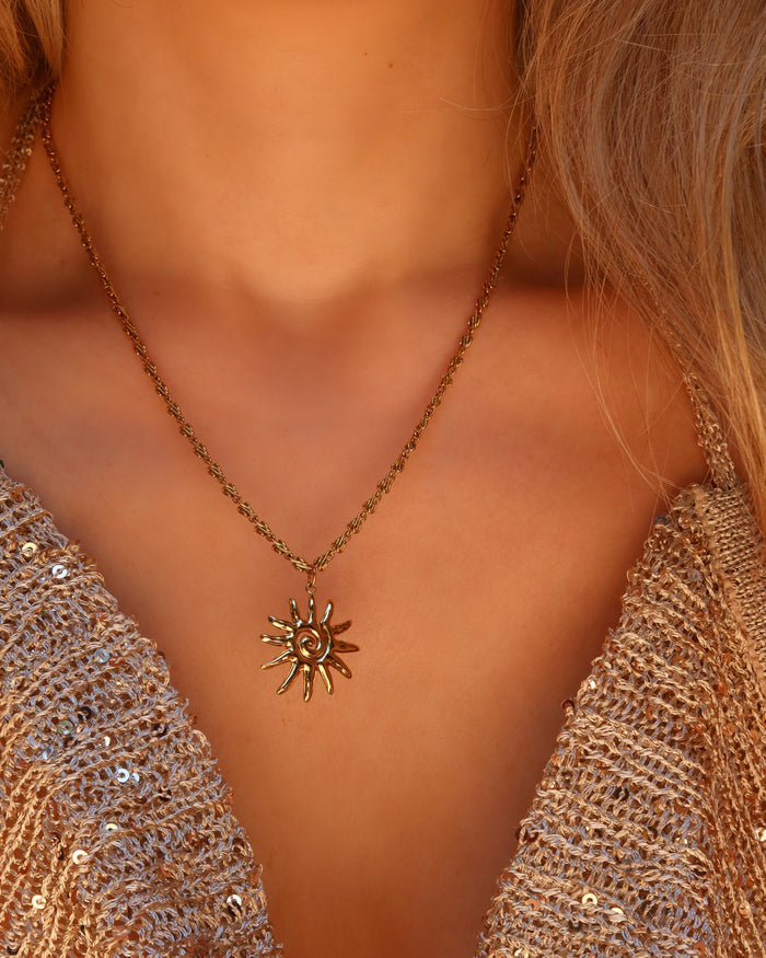 Woman wearing a gold spiral sun pendant necklace made in Greece, Greek jewelry