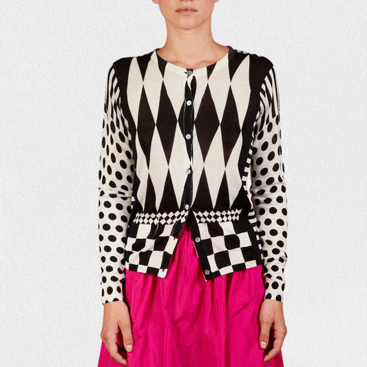 Wearing the IN BED WITH YOU - GEOMETRIC PRINT CARDIGAN by IN BED WITH YOU/CLAUDIOLAI SRL in cotton silk with diamond, checkered, and polka dot designs, paired with a bright pink skirt against a plain white background.