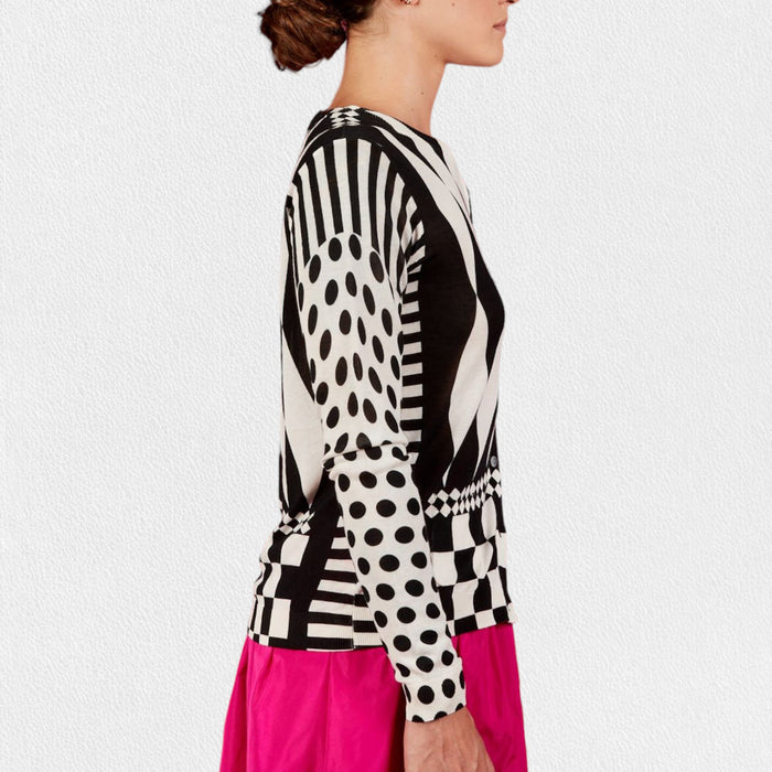 Wearing the IN BED WITH YOU - GEOMETRIC PRINT CARDIGAN by IN BED WITH YOU/CLAUDIOLAI SRL in cotton silk with diamond, checkered, and polka dot designs, paired with a bright pink skirt against a plain white background.