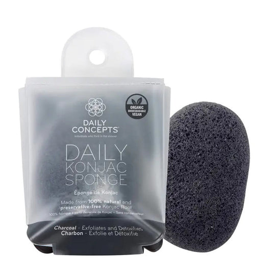 The black DAILY CONCEPTS KONJAC SPONGE - CHARCOAL sits next to its clear packaging, showcasing its detoxifying, organic, vegan benefits and that it’s made from 100% natural konjac root.