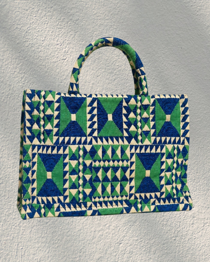 A woven tote bag with a geometric pattern in blue, green, and cream, featuring two top handles, carried by actress Ashley Park in Netflix Emily in Paris handbag