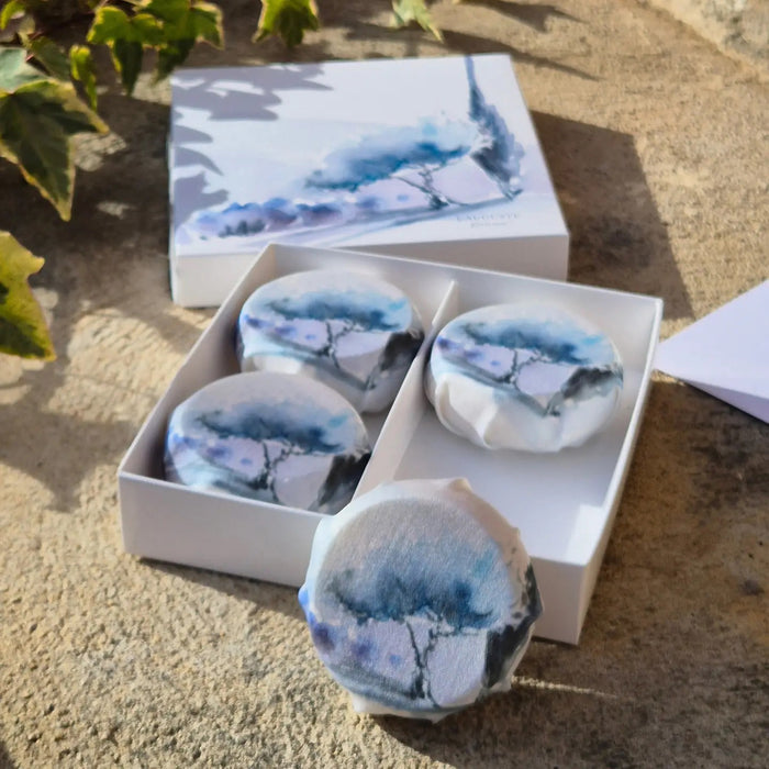 Four round, creamy white L'AUGUSTE PROVENCE artisanal lavender soaps are elegantly boxed—a beautiful Provence gift by L'AUGUSTE PROVENCE, ready to delight any recipient.