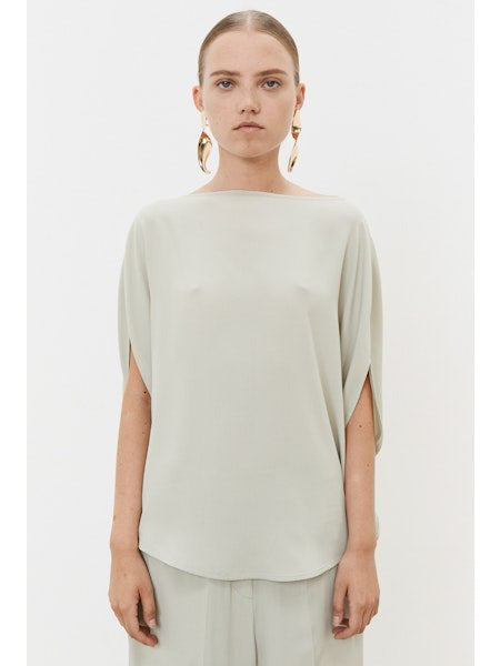 A person with tied-back hair faces away, wearing a light gray MEIMEIJ Silk Blend Top with minimalist design and elegant acetate-silk earrings against a plain white background.
