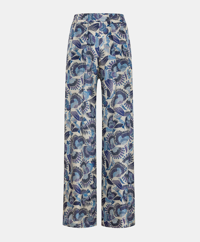 The MOMONI - ASPEN PANT features a luxurious haboutai silk fabric with a geometric pattern of squares and rectangles, adorned with vibrant floral motifs and architectural designs in colors like yellow, green, and blue.