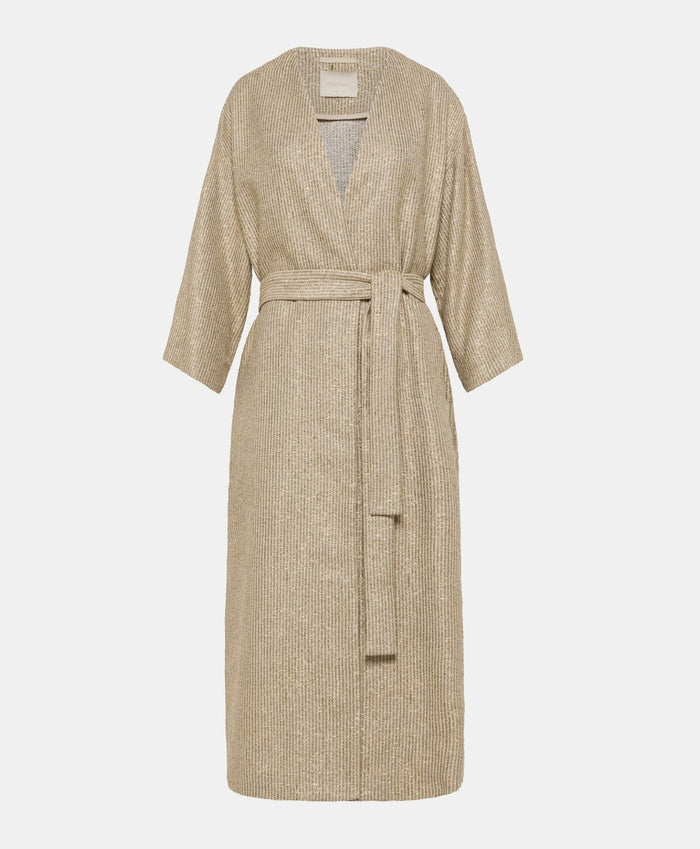 A woman poses against a plain light background wearing the MOMONI - CALL Lightweight Coat in Lurex Basketweave over a patterned shirt and loose, high-waisted beige wide-leg pants. She has straight dark hair and brown shoes.