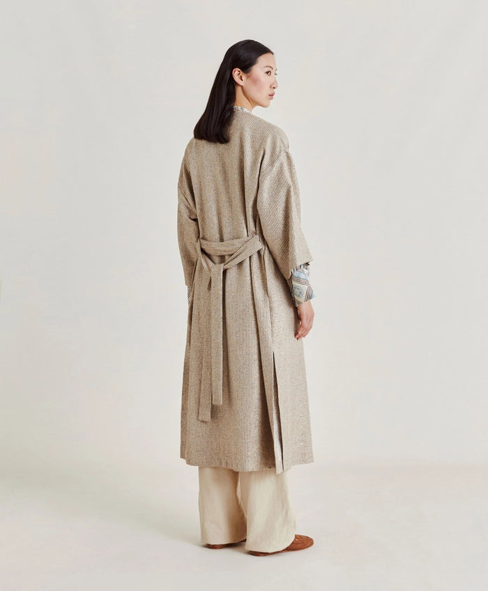 A woman poses against a plain light background wearing the MOMONI - CALL Lightweight Coat in Lurex Basketweave over a patterned shirt and loose, high-waisted beige wide-leg pants. She has straight dark hair and brown shoes.