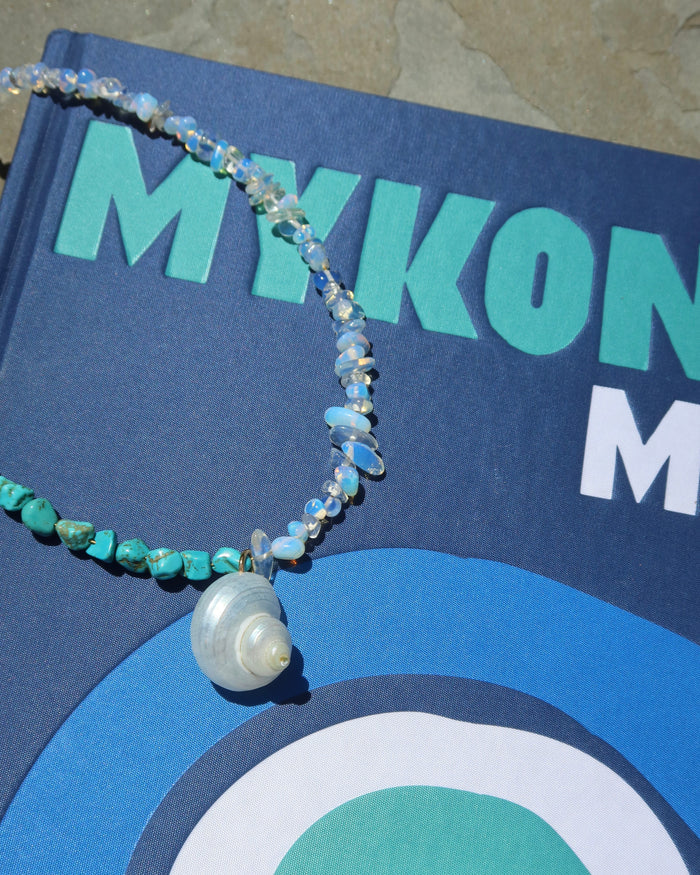 Beaded necklace with howlite and moonstones with a shell pendant on a blue Mykonos Muse book