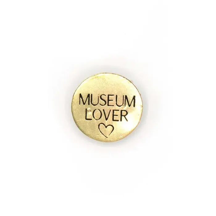 A brass lapel pin that has the phrase Museum Lover inscribed onto it with a heart underneath.