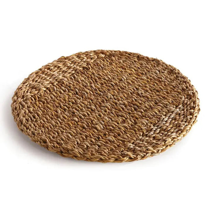 The NAPA HOME AND GARDEN - SEAGRASS ROUND PLACEMAT, featuring a textured, natural brown color, beautifully complements the elegance of Italian ceramics on a white background.