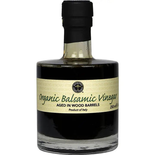 A bottle of USDA Certified Organic Balsamic Vinegar from RITROVO, aged in wood barrels. The dark brown liquid is contained in a clear, short bottle with a black cap, and a beige label displays information, including "250 mL" and "Made in Italy.