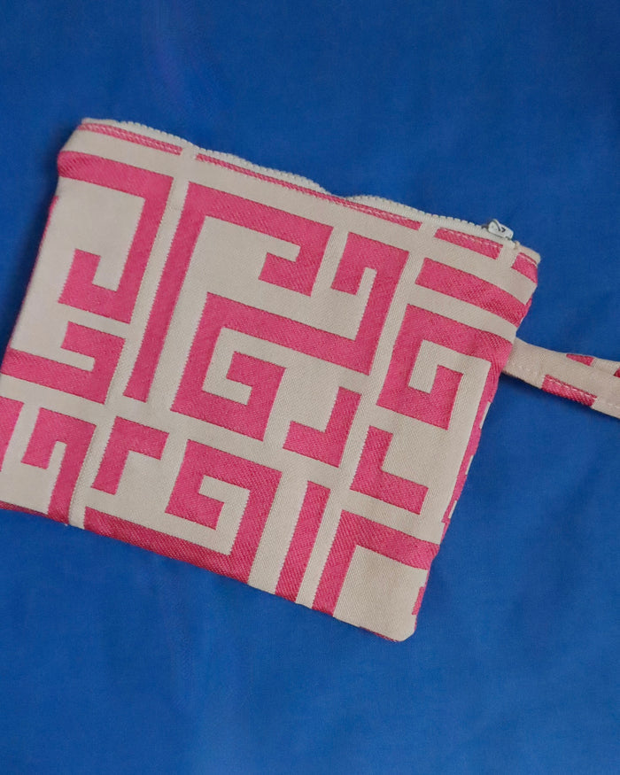 A small zippered pouch with a pink and off-white Greek key pattern, shown on a solid blue background.
