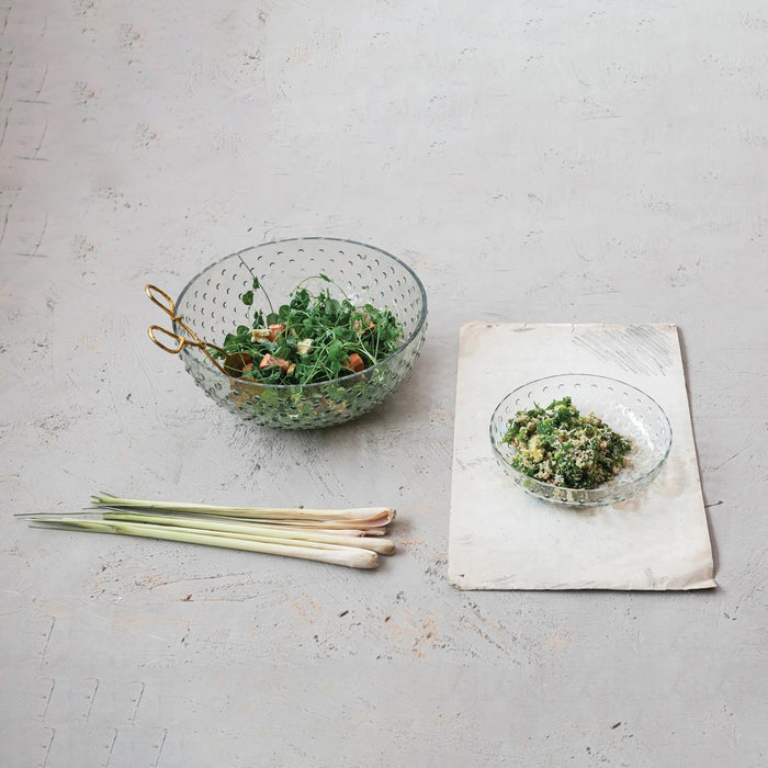The CREATIVE COOP RECYCLED GLASS HOBNAIL LOW BOWL features a textured, dimpled surface with a scalloped edge. This elegant serveware piece is made from transparent recycled glass and offers a simple design.