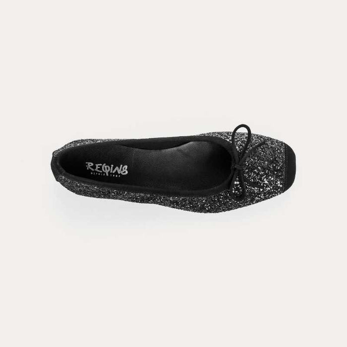 The REQINS Harmony Sequin Ballerina Flats in Noir feature black sequins, black toe caps, and small bows—bringing a touch of everyday luxury against a plain light background.