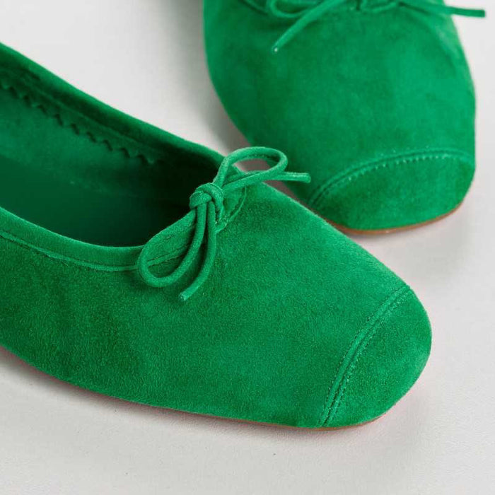 Top view of the REQINS - HARMONY suede ballerina flat in Gazon Green, featuring a small bow on the toe, photographed on a plain light background.