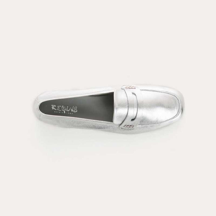The REQINS HEMA Metallic Loafer in Silver features shimmering leather, a low brown heel, classic stitching, and a penny slot detail on the upper, showcased on a plain light background.