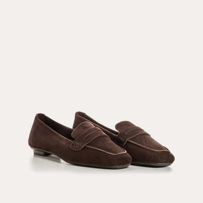 A person stands on a light floor wearing rolled-up blue jeans and REQINS HEMA suede loafers in Marron, showcasing the artisanal craftsmanship of REQINS.