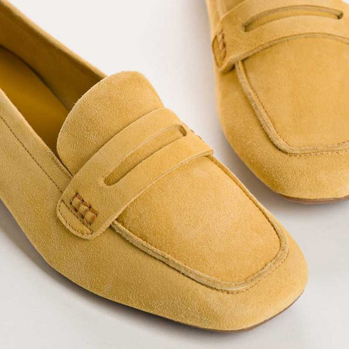 The REQINS - HEMA Suede Loafer in Ochre, expertly crafted by REQINS, features a low heel and a decorative front strap, shown against a plain light background.
