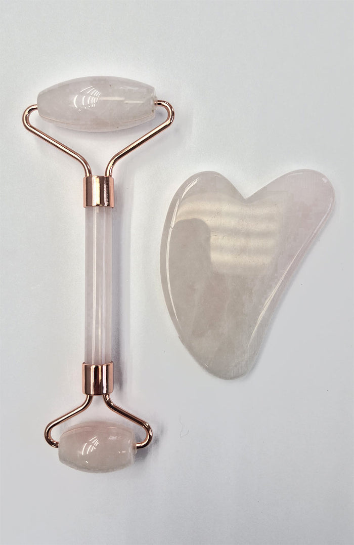 Rose gold facial roller and gua sha tool on a light gray background