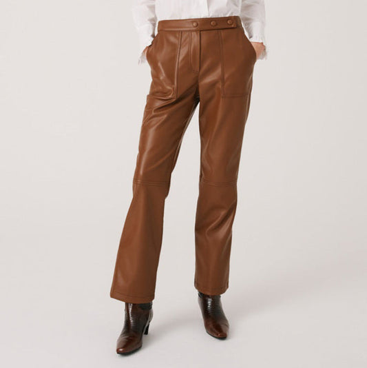 A person wearing high-waisted brown leather pants, a white long-sleeve shirt, and brown heeled ankle boots, standing against a plain light background. The person's face is not visible.