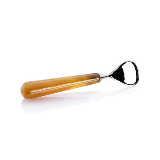 The ZODAX SPIGA BOTTLE OPENER with a gold handle sits on a shiny brass resin plate, displayed on wood next to a glass bottle.
