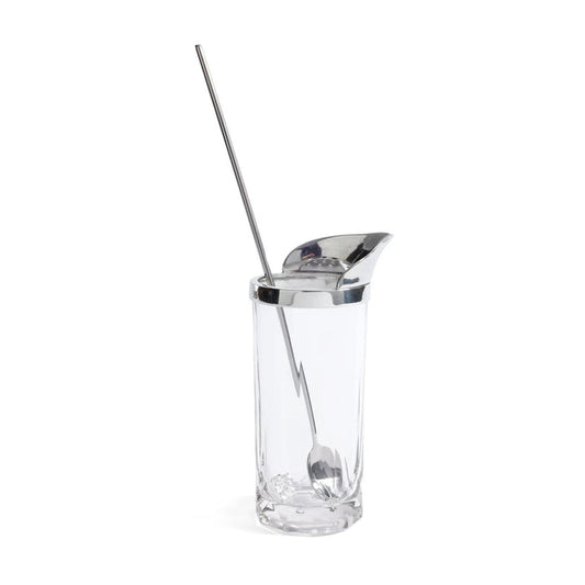 A ZODAX ST. ANTON Pewter and Glass Shaker with Stirrer sits on a woven tray alongside a martini glass and a small tray of almonds, all set against a pale background.