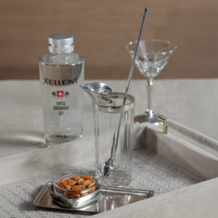The ZODAX ST. ANTON Pewter and Glass Shaker with Stirrer, a 21 oz clear glass container with a metal spout, includes a long metal stirring spoon and straw, all shown upright on a white background.