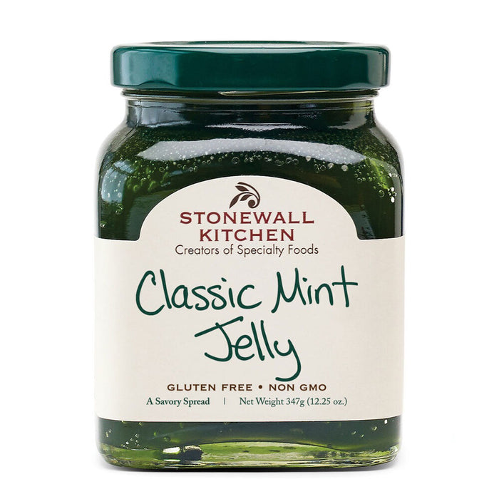 A jar of STONEWALL KITCHEN - CLASSIC MINT JELLY showcases a vibrant green jelly through its clear glass. The label proudly displays "Creators of Specialty Foods," "Gluten Free," and "Non GMO," indicating its quality ingredients. It weighs 347g (12.25 oz) and is topped with a dark green lid, making it an ideal accompaniment for lamb and other hearty meats.