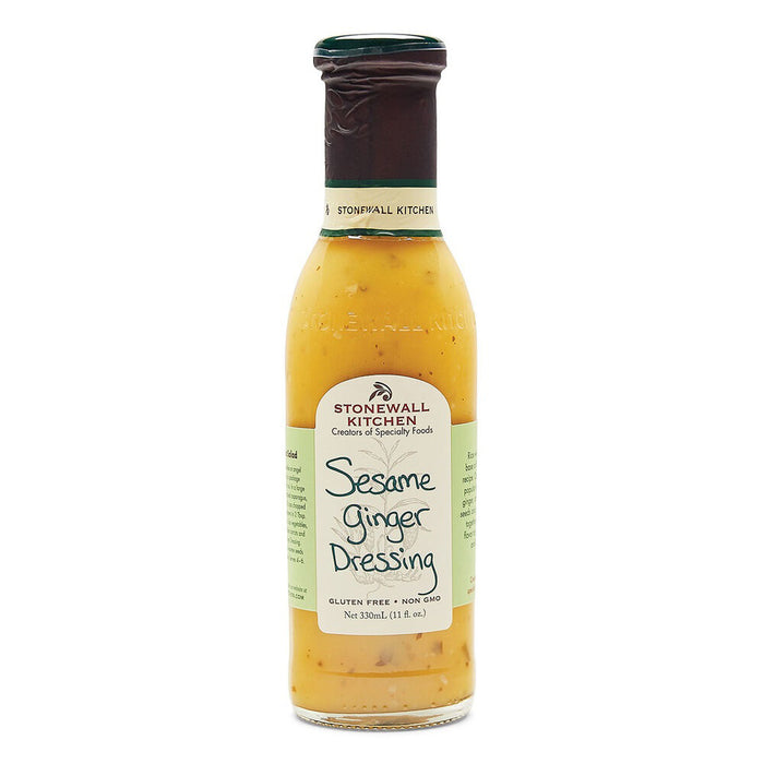 A bottle of STONEWALL KITCHEN - SESAME GINGER DRESSING from Stonewall Kitchen stands against a white background. The label indicates it is gluten-free and non-GMO. Perfect for an Asian-inspired recipe, this salad dressing boasts a light brown hue with visible sesame seeds and hints of rice wine vinegar.