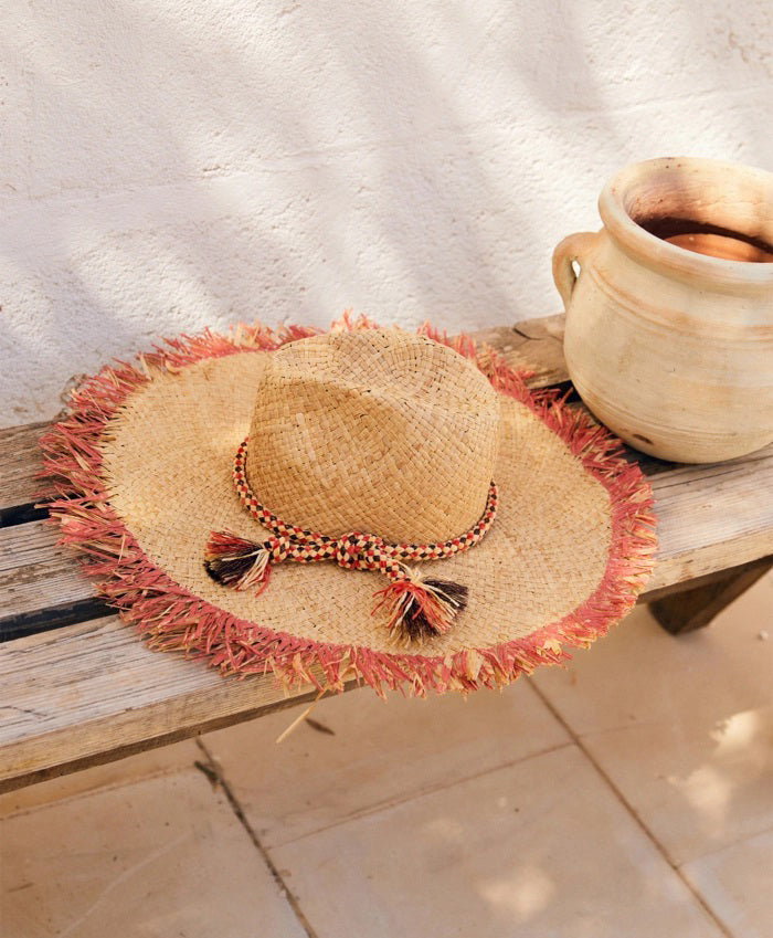 The MOMONI TALLULAH RAFIA SUMMER HAT, crafted in Italy from natural raffia, features a wide fringed brim with a frayed blue edge and a blue braided crown band, displayed on a plain light background.