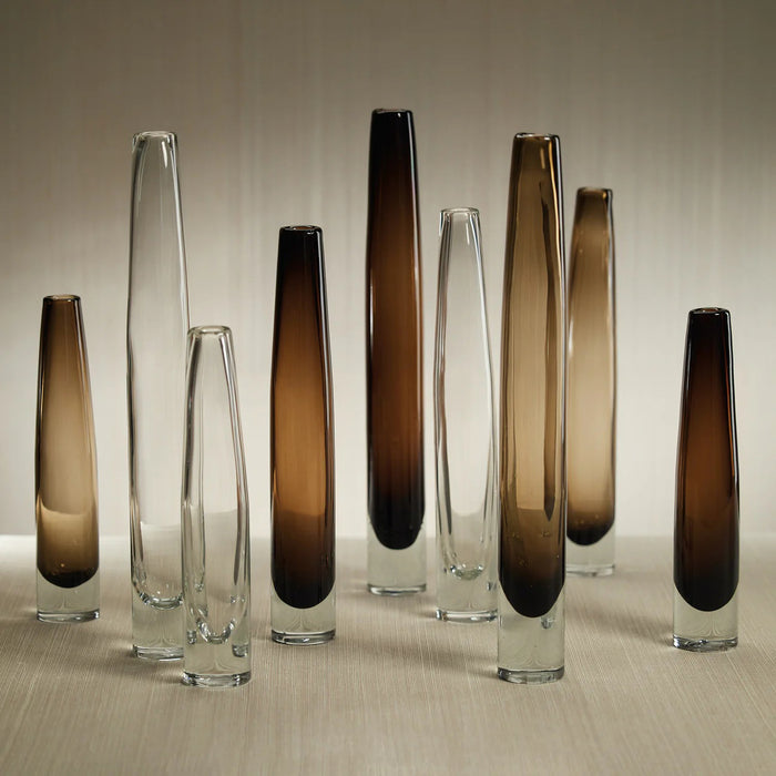 The ZODAX TATE SLIM CLEAR GLASS VASE - SHORT, featuring a narrow neck and wider base, measures 2.5 in x 13.5 in and is shown against a plain white background.