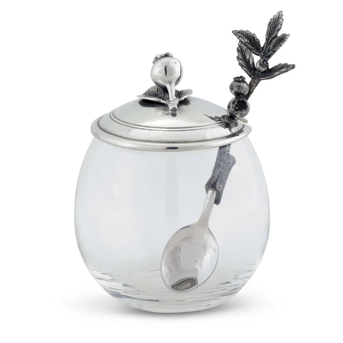 The VAGABOND HOUSE BLUEBERRY JAM JAR features a clear glass body with a silver lid adorned with intricate pewter birds and leaves, paired with a spoon that has a branch-like handle, offering elegance by the brand VAGABOND HOUSE.
