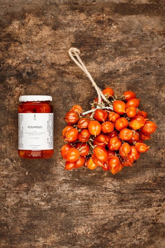 A glass jar of VESUVIO PIENNOLO TOMATOES from ZIA PIA IMPORTS, featuring cherry tomatoes in water. The jar sports a white label with simple decorative designs and reads "Vesuviello con Pomodorino del Piennolo del Vesuvio DOP in acqua.