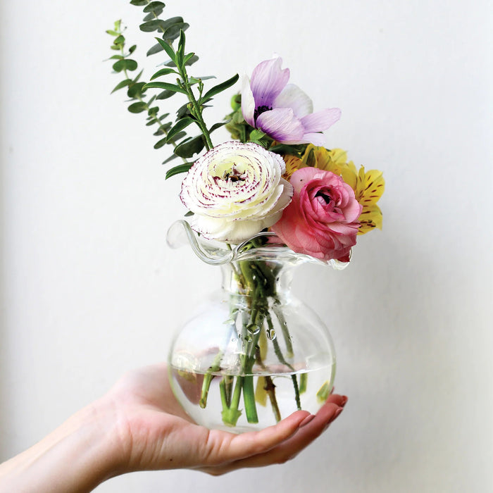 The VIETRI - HIBISCUS BUD VASE CLEAR features a round base and wide, wavy rim, expertly crafted by Tuscan artisans. Displayed against a white background, this clear glass bud vase highlights VIETRI's elegant Italian design.