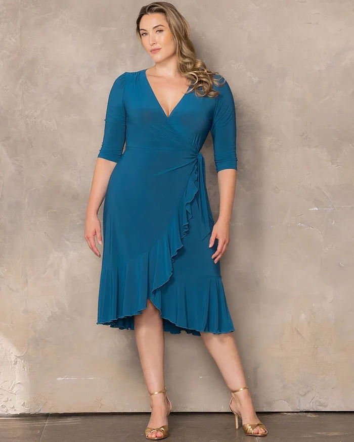 Whimsy Wrap Dress - Sale! in Aegean Blue. Model in a blue ruffle wrap dress and gold heels in front of a beige background.