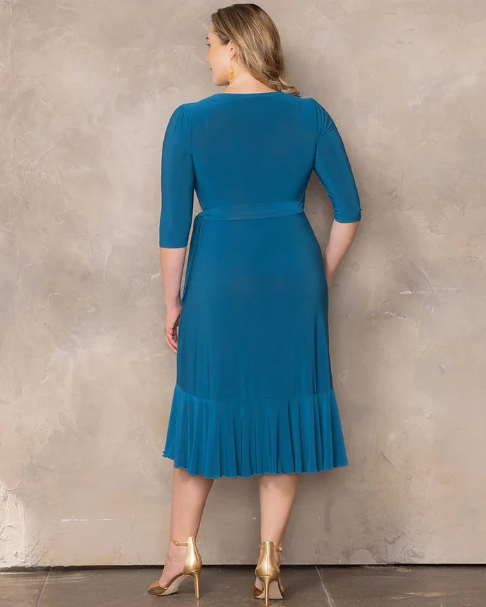 Whimsy Wrap Dress - Sale! in Aegean Blue. Model in a blue ruffle wrap dress and gold heels in front of a beige background.