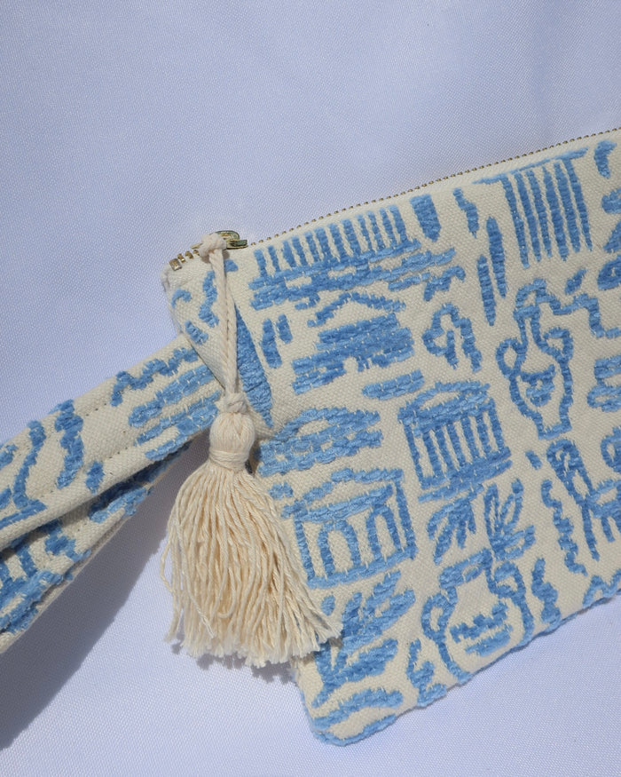 Wristlet clutch bag with a light blue Greece inspired print featuring the Parthenon, owls, vases, ancient Greek scultures, olive trees and more. Made in Greece with a tassel, zipper closure, and wrist strap